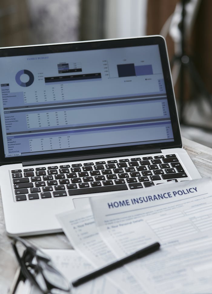 Services Close-up of home insurance policy papers with a laptop displaying financial analysis.